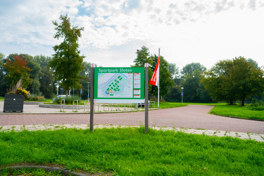 Informatiebord met plattegrond op een grasveld bij een sportpark